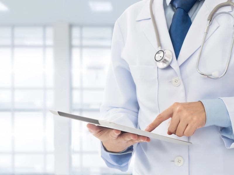 Doctor wearing a stethoscope reviewing a chart on a tablet.