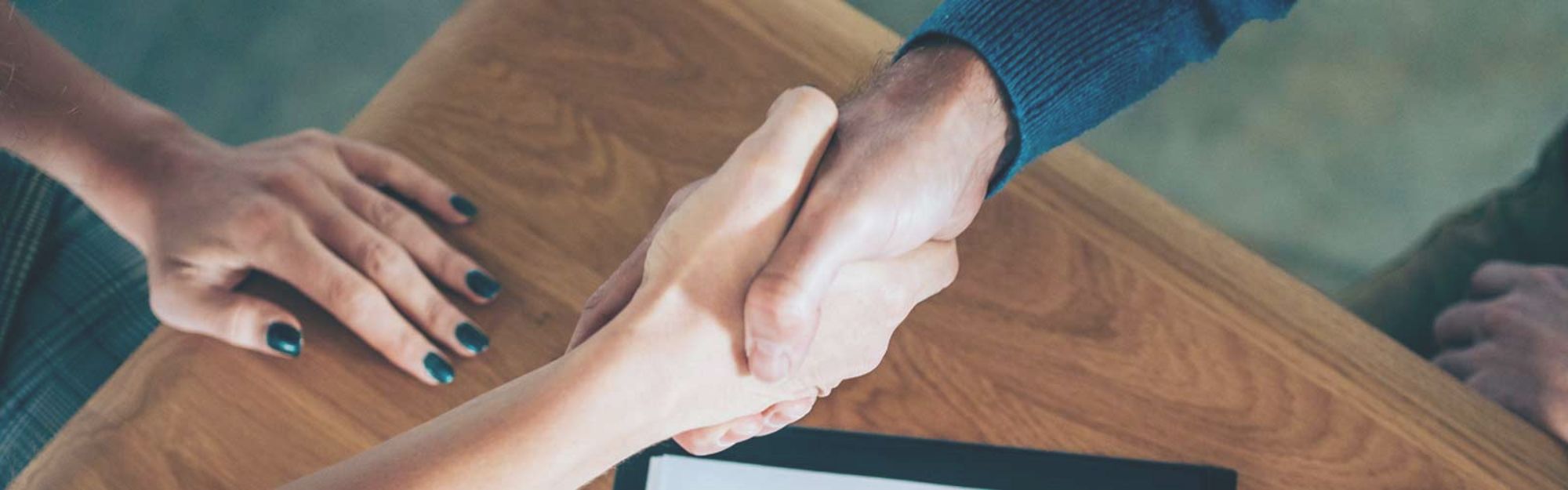 two people shaking hands over a wooden table 